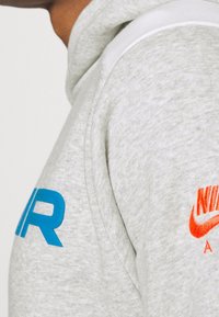 Gray hoodie with a soft texture, featuring blue "AIR" text on the left arm and an orange "NIKE" logo on the right, showcasing a casual design.