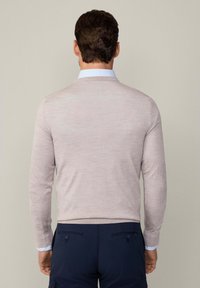 Maglione lavorato a maglia di un delicato rosa con maniche lunghe e scollatura arrotondata, indossato sopra una camicia con colletto di un chiaro blu, abbinato a pantaloni blu navy.
