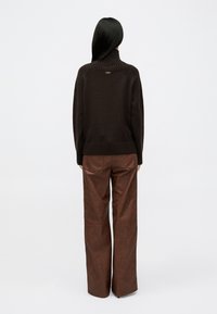 Maglione marrone a maglia con colletto alto e orlo a coste, abbinato a pantaloni larghi in finta pelle marrone con tasche posteriori.