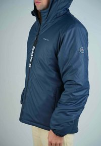 Veste rembourrée bleu marine avec capuche, dotée d'une fermeture éclair à l'avant, de poignets élastiques et d'un patch logo sur la manche. Matériau lisse et imperméable.