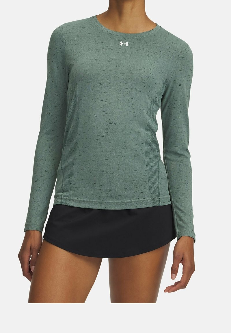 Maglia sportiva a maniche lunghe di colore verde, realizzata in tessuto testurizzato, con collo rotondo e logo sul petto. Abbinata a una gonna nera.
