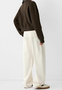 Brun kortad sweatshirt och lösa vita jeans. Texturert tyg, avslappnad passform, med kontrasterande sömmar och beige sneakers.