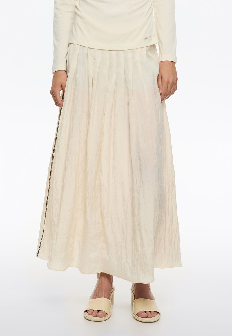 Gonna maxi plissettata di colore avorio, realizzata in un tessuto leggero e testurizzato con cerniera laterale e una leggera lucentezza. Abbinata a sandali beige con zeppa.