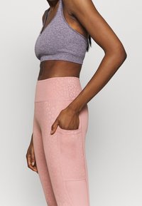 Fialový sportovní crop top a růžové legíny s leopardím vzorem. Legíny mají boční kapsu a hladkou texturu.