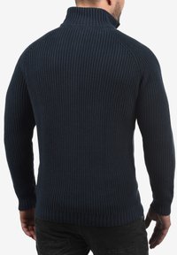Marineblauer gerippter Pullover mit hohem Kragen und langen Ärmeln, der ein strukturiertes Strickmuster aufweist und an den Bündchen und dem Saum eng anliegt.