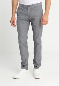 Graue gemusterte Hose im Slim-Fit-Design mit Knopfverschluss und Taschen, kombiniert mit weißen Sneakers.