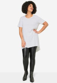 Witte katoenen tuniek met een ronde hals, korte mouwen, asymmetrische zoom, gecombineerd met zwarte nep leren leggings en gestudeerde enkellaarsjes.