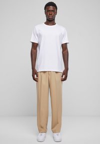 Witte t-shirt met korte mouwen, losse beige broek en witte sneakers. Het t-shirt is eenvoudig, terwijl de broek een ontspannen pasvorm heeft.