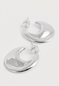 Paari läikivad hõbedast poolkuu kuju kõrvarõngaid, millel on läbipaistvad plastist tagused valgel taustal.