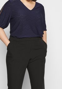 Námořnicky modrý texturovaný top s výstřihem do V a krátkými rukávy, doplněný černými kalhotami se bočními kapsami a přizpůsobeným střihem.