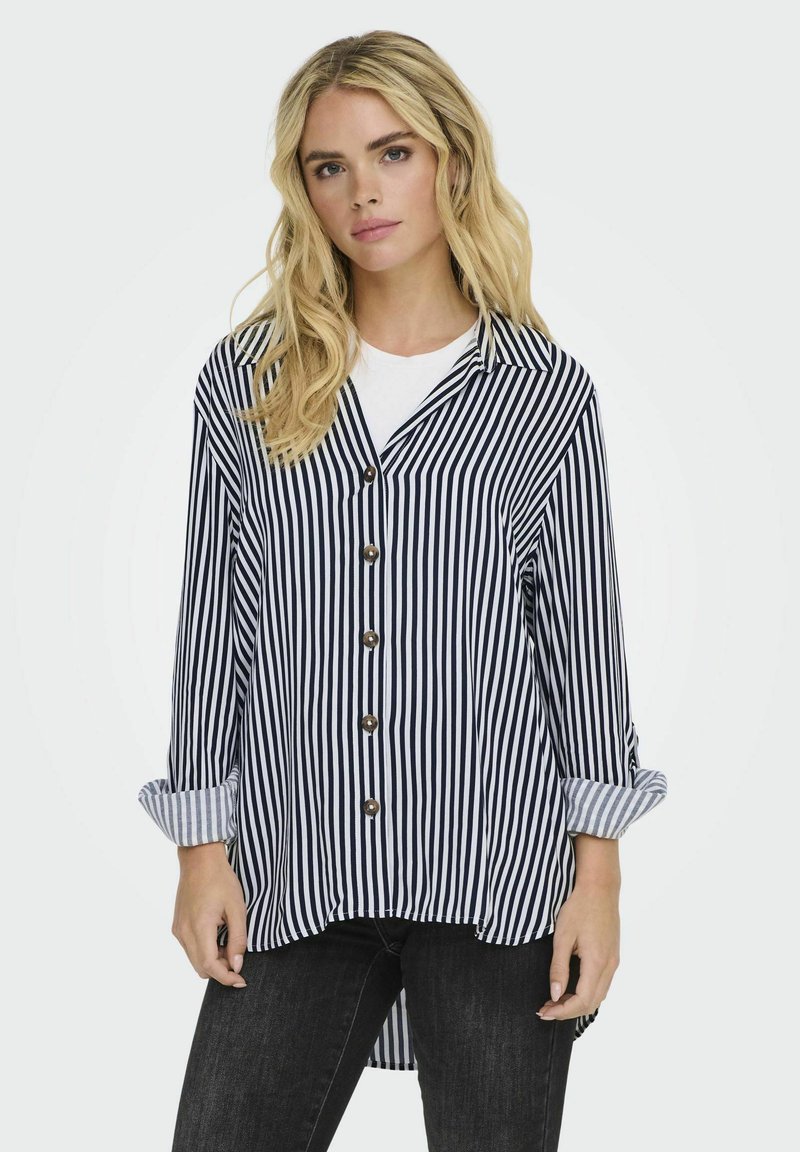 Camisa de rayas en azul marino y blanco con cuello, botones en la parte frontal y mangas enrolladas. Material suave con un corte holgado y un dobladillo trasero más largo.