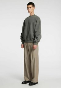 Felpa grigia oversize con scollo rotondo, caratterizzata da polsini e orlo a costine, abbinata a pantaloni beige a gamba larga e calzature nere.