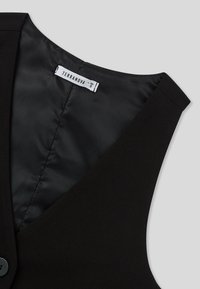 Gilet nero senza maniche con scollatura a V e foderatura interna liscia. Presenta un'etichetta di dimensione marcata 'TERRANOVA' e un dettaglio con un bottone.