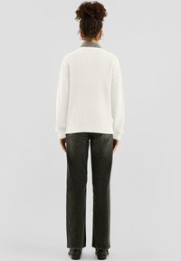 Biały sweter z prążkowanego dzianiny i ciemnozielone jeansy o prostych nogawkach, zestawione z czarnymi butami. Sweter ma wysoki kołnierz i szerokie rękawy.