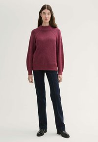 Bordeauxfarbener Rippstrick-Pullover mit hohem Kragen und langen, engen Ärmeln, kombiniert mit dunkelblauen Jeans im geraden Schnitt und schwarzen Knöchelstiefeln.
