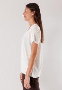 Top bianco a maglia a maniche corte con scollatura a V e orlo a coste, progettato con una vestibilità ampia, abbinato a pantaloni aderenti marrone scuro.