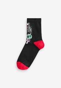 Svart socka med en färgglad grafisk design som visar ett ansikte, gröna och rosa accenter, samt röd tå och häl. Slät tygtextur.