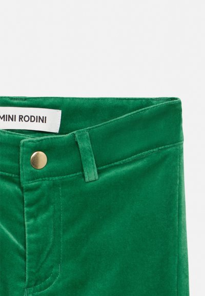Πράσινο παντελόνι από βελούδο με μεταλλικό κουμπί, θηλιά για ζώνη και λευκή ετικέτα Mini Rodini ορατή στο εσωτερικό της μέσης.