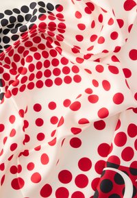 Selymes anyag, krémszínű alapon ismétlődő mintával, piros és fekete pöttyökkel, sima textúrával és élénk színekkel.