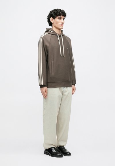 Καφέ φούτερ με κουκούλα και αντίθετες κρεμ ρίγες, τσέπη καγκουρό και κορδόνια. Συνδυάζεται με ανοιχτόχρωμο, φαρδύ παντελόνι και μαύρα παπούτσια.