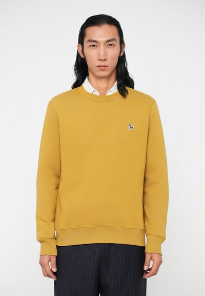 Mustard-colored sweatshirt with a round neckline and long sleeves, featuring a small embroidered logo on the chest. Smooth texture.