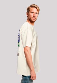 Cream-colored short-sleeve t-shirt with a graphic print on the back featuring blue and green accents. Relaxed fit and soft texture.