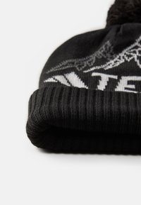Zwarte gebreide beanie met een geribd ontwerp en een omgeslagen rand. Bevat een wit grafisch patroon en een pluizige pom-pom bovenop.
