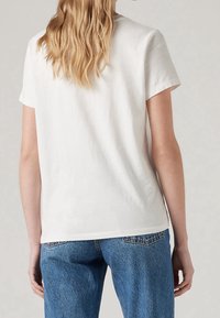 Vit bomullströja med korta ärmar, en avslappnad passform och en rak nederkant, i kombination med blå högmidjade denimjeans.