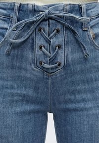 Μπλε τζιν παντελόνι με κορδόνια στο μπροστινό μέρος περασμένα μέσα από μεταλλικά ροδέλες και δεμένα σε φιόγκο στη μέση.