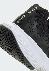 Czarne buty sportowe z siateczkową cholewką, białą podeszwą środkową i wzorzystą podeszwą gumową. Zawierają napis "GAMECOURT 2" na pięcie oraz otwory wentylacyjne.