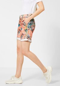 Barevné vzorované šortky s broskvovým podkladem, které mají designy tropických listů. Otočené lemy a boční kapsy pro funkčnost.