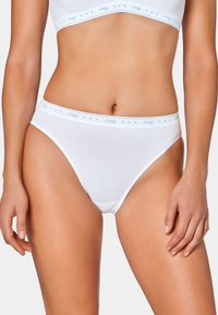 Slip di cotone bianco con una texture liscia e lati stretti. Presenta un elastico alla vita con un logo azzurro e dettagli decorativi.