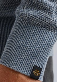 Blauer Strickpullover mit strukturiertem Muster und Rippbündchen. Enthält ein schwarzes Etikett mit dem aufgenähten Branding "PME LEGEND" an der Seite.