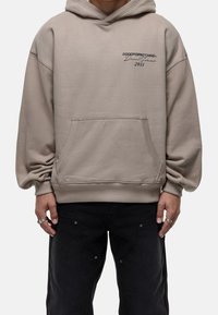 Felpa beige con tasca frontale, polsini e orlo a costine, con dettaglio del logo ricamato in blu scuro. Tessuto morbido con vestibilità comoda.