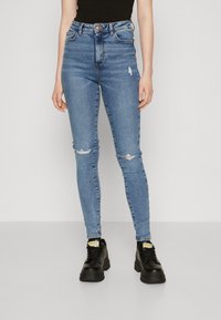 Jeans blue cu talie înaltă și croială slim, av�ând zonele genunchilor deteriorate. Asortați cu adidași negri, cu talpă groasă. Design simplu, casual.