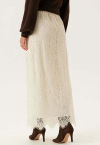 Spetsmaxikjol i off-white med intrikata blommönster och v�ågig nederkant, i kombination med bruna klackstövlar. Strukturerad tyg.
