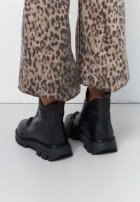 Zwarte enkellaarsjes met een structuurleer afwerking, voorzien van een chunky zool en een rits aan de zijkant. G draagt ze met een leopardprint wijde broek.