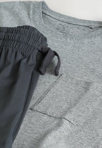 Gråstribet T-shirt med lomme, der er parret med mørkegrå bukser med elastisk talje. Stoffet ser blødt og let ud, hvilket giver en afslappet komfort.