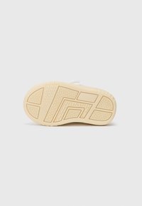 Sneakersula i beige gummi med strukturerat greppmönster. Platt design med djärva vinklade former och djupa spår för dragkraft.