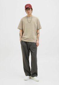Beige Baumwoll-T-Shirt mit kurzen Ärmeln, graue, lockere Hose und weiße Sneaker; dazu eine rote Mütze mit einem weißen Logo.