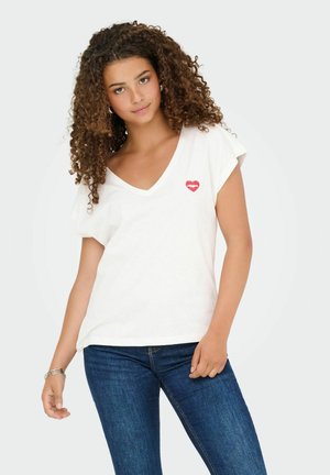 Biała koszulka z krótkim rękawem z dekoltem w serek, z czerwoną grafiką w kształcie ust na lewej piersi. Połączona z ciemnoniebieskimi dżinsami.