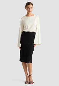 Witte lange mouwen top met een ronde hals gecombineerd met een aansluitende zwarte pencil skirt met een split, gedragen met zwarte hoge hakken sandalen.