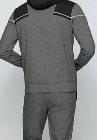 Sudadera gris con detalles negros, tejido texturizado y ribetes blancos. Presenta mangas largas y un corte relajado, combinada con pantalones grises a juego.