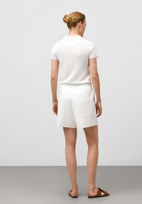 Vit polo t-shirt med korta ärmar, ihop med vita shorts som har en bakficka. Bärs med bruna slidesandaler.