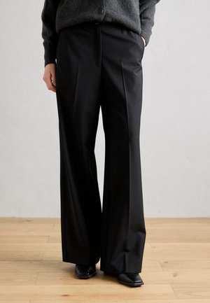 Weite schwarze Hosen aus glattem Stoff, mit einer vorderen Falte und maßgeschneidertem Design, kombiniert mit einem grauen strukturierten Pullover.