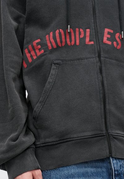 Hanorac negru cu fermoar, realizat dintr-un material moale, având o buzunar frontal, șnururi gri și un text roșu îndrăzneț pe piept care spune "THE KOOPLES."