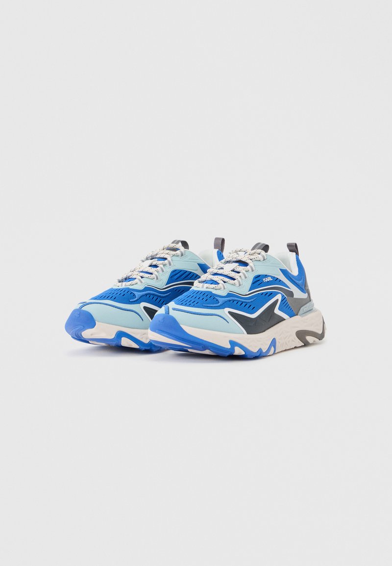 Par de zapatillas deportivas azules y blancas con diseño de cordones, suela texturizada y detalles en negro y gris, mostradas sobre un fondo blanco.