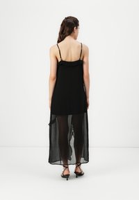 Robe noire à fines bretelles, décolleté ondulé, tissu transparent, design long et fluide, avec un ourlet légèrement évasé en bas.
