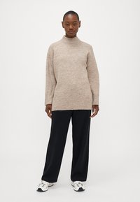 Maglione beige lavorato a maglia con colletto alto, maniche lunghe e polsini a coste, abbinato a pantaloni black a gamba larga e sneaker bianche.