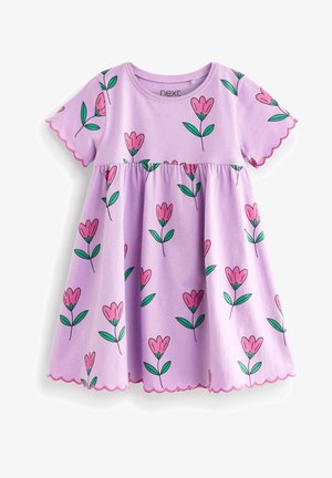 Peuter draagt een lavendelkleurige jurk met roze en groene bloemenprint en meerkleurige metallic sandalen, staande op een lichte achtergrond.